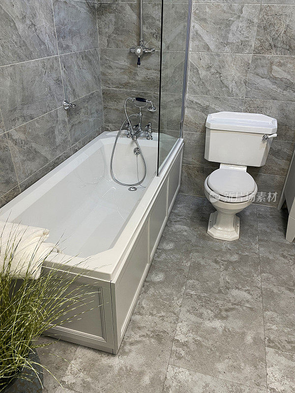 白色/灰色大理石墙砖的豪华浴室套房，白色陶瓷浴缸，镀铬维多利亚式龙头和淋浴管道，玻璃淋浴屏，手柄冲水马桶